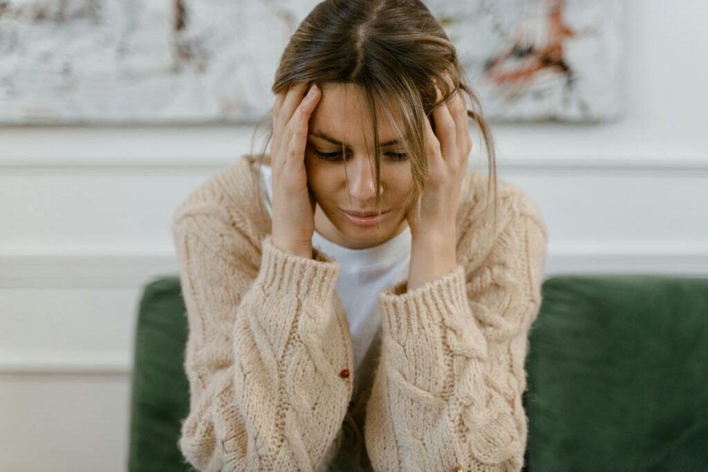 pexels-photo-7699482-7699482 A woman sitting on a sofa holding her head, expressing stress and frustration indoors.
